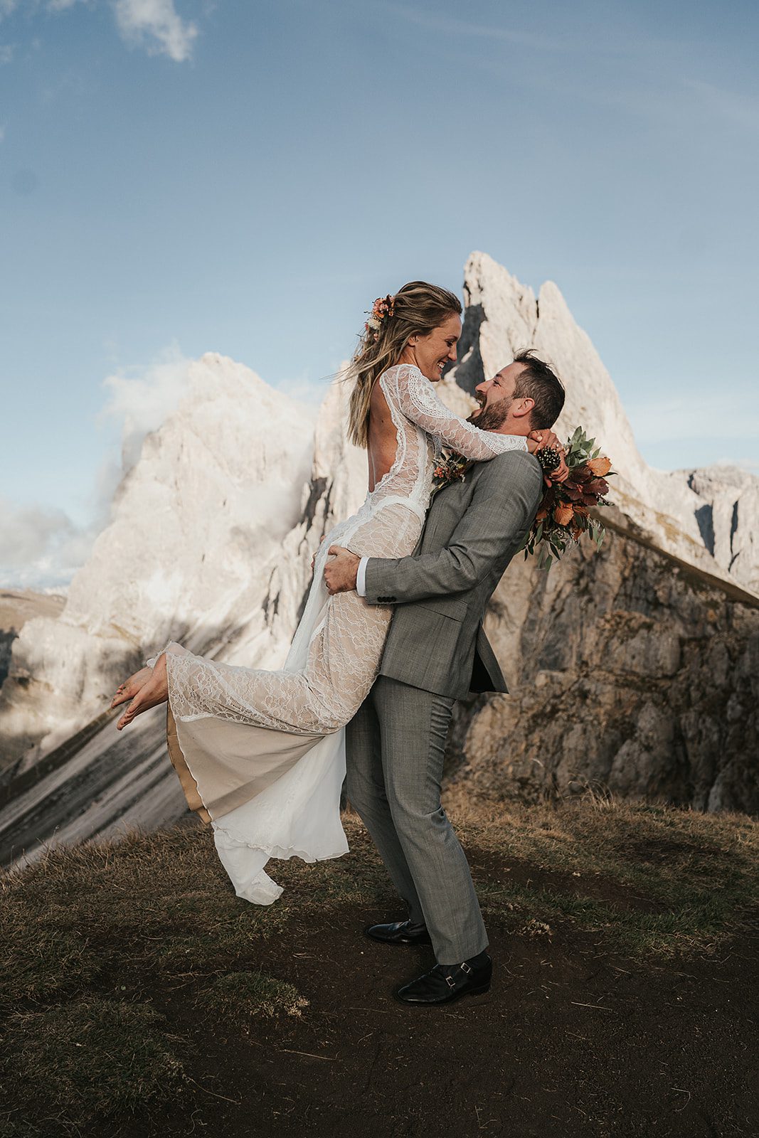 Groom carries bride up in his arms with the view of the breathtaking Seceda mountain in Italy, captured by Blitzkneisser
