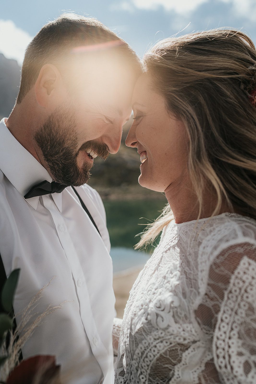 Close-up shot of the bride and groom resting their foreheads gently against each other as they smile while the sun gleamed behind them