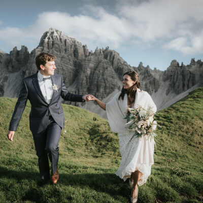 How to Plan The Perfect Mountain Elopement + Locations: Bide and groom smiling at each other as they hold hands while walking along the mountain during their elopement shoot