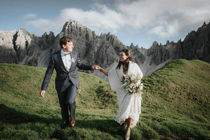 How to Plan The Perfect Mountain Elopement + Locations: Bide and groom smiling at each other as they hold hands while walking along the mountain during their elopement shoot